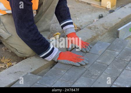 Professionelle Arbeiter Schichten installieren Mauerwerk grauen Beton Ziegel der Straße in der Stadt Stockfoto
