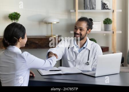 Lächelnder afroamerikanischer Arzt und indischer Patient schüttelt die Hände Stockfoto