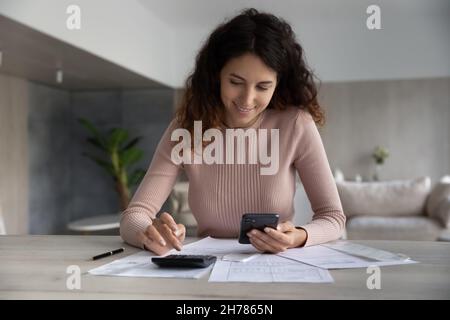 Lächelnde Frau mit Smartphone und Rechner, die mit Finanzdokumenten arbeitet Stockfoto