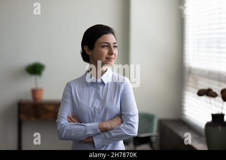 Selbstbewusste indische Geschäftsfrau mit gekreuzten Armen und Blick in die Ferne Stockfoto