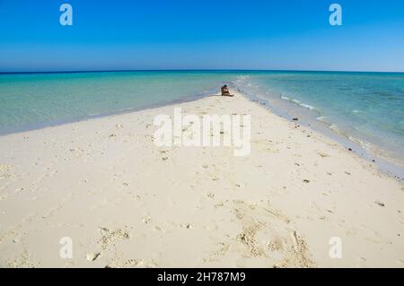 Ägypten, Sinai Desert Peninsula , Ras Mohammed, Frau in ihren Zwanzigern sitzt allein auf einem langen Stück verlassenen Strand endlosen Horizont von Ozean und Himmel in Stockfoto