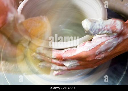 Eine europäische Töpferin in ihrer Werkstatt formt Ton auf einem Töpferrad. Nahaufnahme ihrer Hände, die Bewegung zeigen Stockfoto