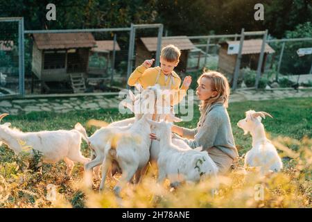 Fröhliche, fröhliche Mutter und Sohn füttern und pflegen Ziegen auf dem Bauernhof. Stockfoto