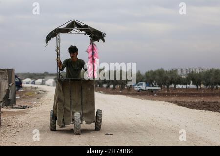 10. November 2021, Azaz, Gouvernement Aleppo, Syrien: Aleppo, Syrien. 10. November 2021. Ein Straßenhändler, der im Flüchtlingslager Al-Zaytoun am Rande der von Rebellen gehaltenen Stadt Azaz im Norden von Aleppo Zuckerwatte verkauft, umgeben von Kindern. In Olivenhainen entlang der türkischen Grenze wurden Zelte aufgebaut, wobei die Bewohner der informellen Siedlung und ihre Kinder mit minimalen Infrastrukturen und Möglichkeiten sowie Platzmangel zu kämpfen haben (Foto: © Zakariya Yahya/IMAGESLIVE via ZUMA Press Wire) Stockfoto