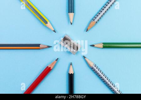 Bleistiftspitzer aus Metall mit acht verschiedenen Graphitstiften, radial auf blauem Hintergrund gesetzt Stockfoto