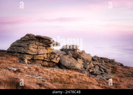 Über einem Wolkenmeer auf dem Brocken im Harz, Nationalpark Harz, Sachsen-Anhalt, Deutschland. Rosa Sonnenuntergang Himmel und Felsformationen. Stockfoto