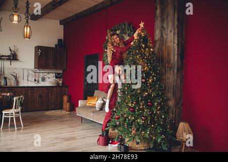 Glückliche Frau und Ehemann in passenden Kleidern, die am Weihnachtsabend zusammen mit dem kunstvollen Heim helfen Stockfoto