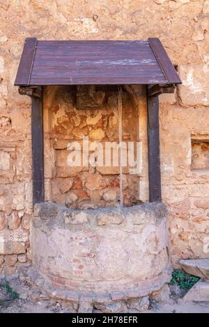 Alter Brunnen zum Wasserschöpfen, an einer Steinmauer befestigt Stockfoto