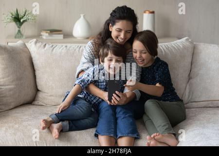 Mama und Kinder schauen auf den Handybildschirm und lachen Stockfoto