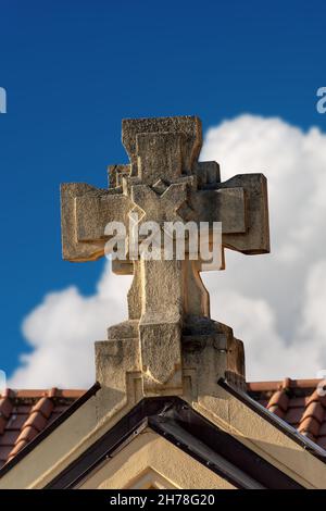 Detail eines christlichen Steinkreuzes auf einem blauen Himmel mit Wolken, religiöses Symbol. Kirche des Heiligen Herzens in La Spezia, Ligurien, Italien Stockfoto