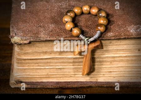 Tau, Holzkreuz in Form des Buchstabens t (religiöses Symbol des heiligen Franziskus von Assisi) mit Rosenkranz auf einer alten Heiligen Bibel Stockfoto