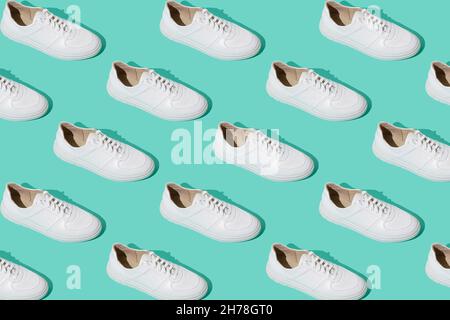 Weißes Sneakers-Muster auf mintblauem Hintergrund. Die Schuhe sind bequem und lässig. Hintergrund für einen Schuhladen. Ein paar neue Schuhe. Stockfoto