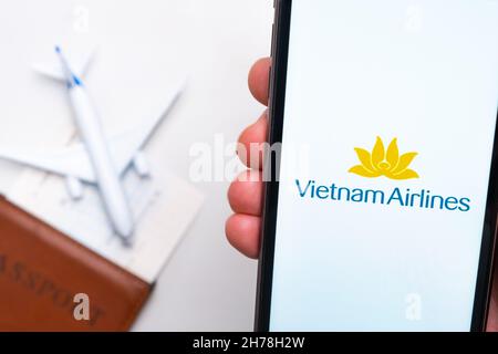 VietnamAirlines App auf einem Smartphone-Bildschirm in mans Hand. Ein Spielzeugflugzeug, Reisepass und Tickets stehen auf dem Tisch. November 2021, San Francisco, USA Stockfoto