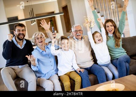 Eine Familie mit mehreren Generationen, die Fußball im Fernsehen sieht und ein Tor feiert, sitzt auf der Couch im Wohnzimmer Stockfoto