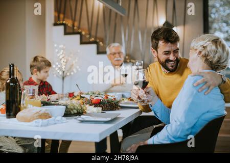 Glückliche Familie, die zu Hause ein Abendessen mit Rotwein zu sich nehmen kann Stockfoto
