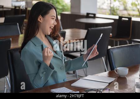 Aufgeregt fröhlich junge Geschäft asiatische Frau mit Faust nach oben erhalten gute Nachrichten auf digitalen Tablet und Schreien im Büro Stockfoto