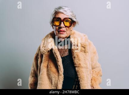 Bild einer schönen und eleganten alten Influencer-Frau. Coole Großmutter posiert im Studio und trägt modische Kleidung Stockfoto