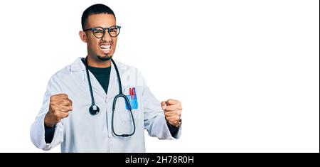 Junger afroamerikanischer Mann mit Ärzteuniform und Stethoskop wütend und verrückt Heben Fäuste frustriert und wütend beim Schreien vor Wut. Wut ein Stockfoto