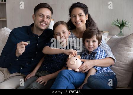 Schönes Paar und Kinder sitzen auf dem Sofa mit Sparschwein Stockfoto