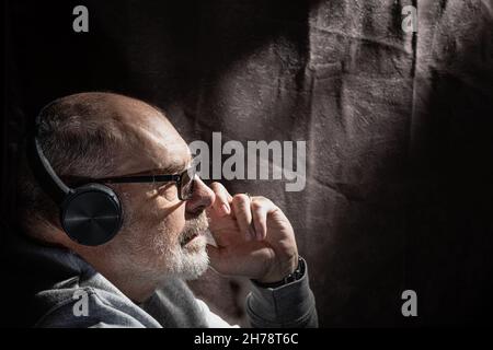 Flaches Porträt eines grauhaarigen Mannes, der über Kopfhörer Musik hört Stockfoto