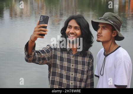 Zwei männliche Freunde, die Spaß haben, während sie zusammen Selfie am See machen Stockfoto