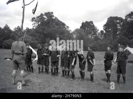 1938, historisch, Junge Pfadfinderlager, Gottesdienst, Felbridge, Surrey, England, Großbritannien. Draußen auf einem Feld, eine Gruppe von Jungen Pfadfinder - ursprünglich bekannt als Wolf Jungen - Line-up mit ihrem Pfadfinder Meister für frühe Morgengebete. Stockfoto