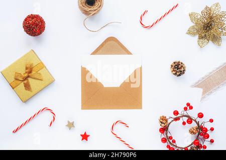 Öffnen Sie einen braunen Umschlag mit einer weißen Karte und Weihnachtsdekorationen, Süßigkeiten und einer Geschenkbox auf weißem Tischhintergrund. Draufsicht, flach liegend, Kopierer Stockfoto