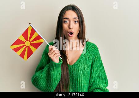 Junge hispanische Mädchen hält mazedonische Flagge verängstigt und erstaunt mit offenem Mund für Überraschung, Unglauben Gesicht Stockfoto