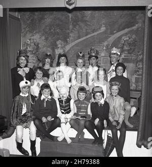 1965, historisch, sitzt zusammen auf einer kleinen Bühne, großes Lächeln von einer Gruppe von Kindern aus einem Jugendzentrum in ihren Kostümen für das Stück, Alice in Wonderland, Fife, Schottland, Großbritannien. Stockfoto