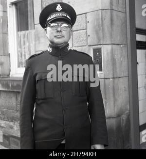 1965, vor einem Gebäude, steht ein Soldat der Heilsarmee in seiner Uniform und seinem Hut stolz aufrecht für sein Foto, Fife Scotland, Großbritannien. Soldaten der Heilsarmee sind Christen, die einen bestimmten Einberufenen oder Versprechen in Bezug auf Lebensstil und Glauben unternommen haben und die Uniform als sichtbares Zeichen ihres Glaubens tragen. Offiziere, Soldaten und Anhänger werden als Salvationisten bezeichnet. Booth wurde 1865 in London von William Booth und seiner Frau Catherine als Wohltätigkeitsorganisation gegründet, um den Armen und Bedürftigen „Erlösung“ zu bringen. 1878 führte Booth die militärische Struktur ein, die sich traditionell fortsetzte. Stockfoto