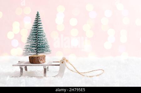 Spielzeug Tannenbaum auf einem Schlitten auf einem verschneiten Hintergrund. Wunderschöne Winterpostkarte. Konzept für Weihnachtsferien, Geschenklieferung. Platz kopieren, Bokeh. Stockfoto