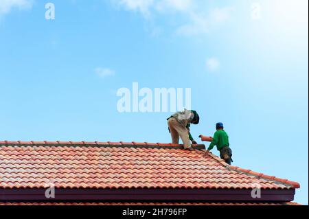 Zwei asiatische Konstrukteure installieren Dachziegel auf dem Dach im Bau. Dachkonstruktion. Stockfoto