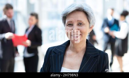 Glückliche erfolgreiche reife asiatische Geschäftsfrau posiert vor Kollegen im Geschäftsaufbau Stockfoto