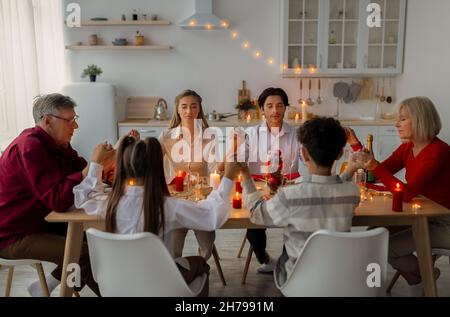 Eine Familie mit mehreren Generationen hält sich die Hände und betet vor dem Thanksgiving- oder Weihnachtsessen, sitzt drinnen am Tisch Stockfoto