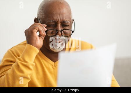 Senior African Man Swinting Eyes Lesepapiere Tragen Von Brillen In Innenräumen Stockfoto
