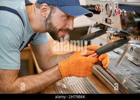 Lächelnder junger Mann, der die Kaffeemaschine im Café repariert Stockfoto