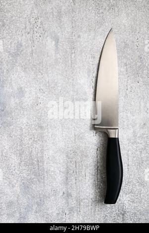 Großes, professionelles Küchenmesser auf einem grauen Betonhintergrund mit Platz für Text, Draufsicht Stockfoto