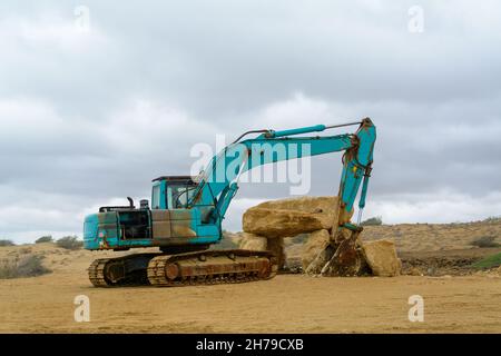 Rückansicht eines rostblauen Industriebaggers, der am Strand mit bewölktem Himmel in der Provinz chabahar, iran, geparkt ist Stockfoto