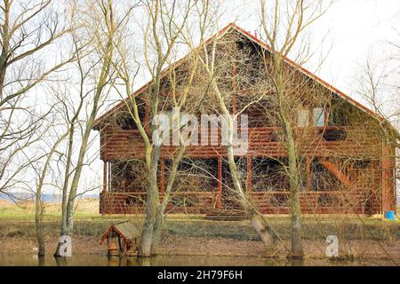 Einsames zweistöckiges Landhaus aus Holz, Ferienhaus, Villa mit Gießdach am Ufer eines Teiches, Fluss, See mitten im Herbstwald. Croft, Crofter' Stockfoto