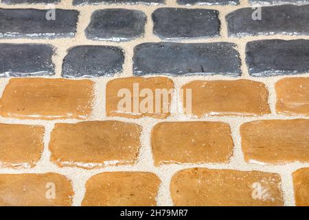 Die Textur eines Fragments eines farbigen Pflasters aus gelbem und grauem Stein. Mosaikmuster. Nahaufnahme. Speicherplatz kopieren. Stockfoto