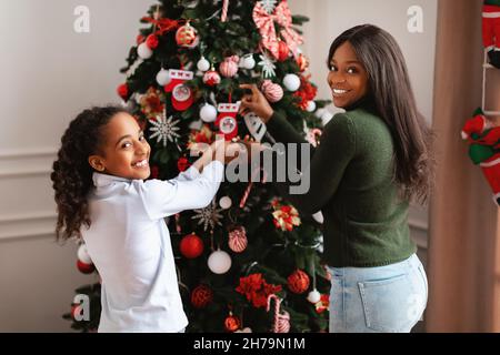 Glückliche schwarze Frau und Mädchen dekorieren Weihnachtsbaum, Blick zurück Stockfoto