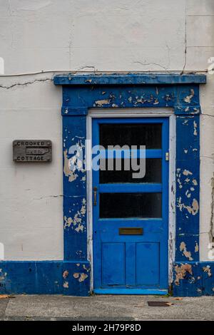 Schiefe Hütte Schild, alte verfallene Tür auf einem Häuschen blau gestrichen mit abblätternder Farbe, Hausname schiefe Hütte Schild. Stockfoto