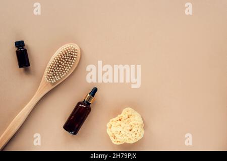Natürliche Bio-Kosmetikprodukte, Öl, Serumflasche, Pinsel und Meeresschwamm auf beigem Hintergrund. Draufsicht, flach liegend, Kopierbereich. Stockfoto