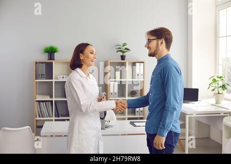 Freundliche, fröhliche Ärztin begrüßt und schüttelt die Hände mit dem Patienten während des Treffens in der Arztpraxis. Stockfoto