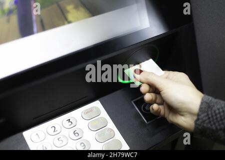 Eine weibliche Hand, die eine Kreditkarte in einen Geldautomaten steckt Stockfoto