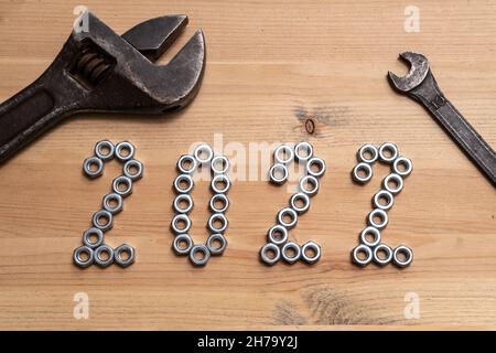 Neujahr 2022 die Zahlen sind mit Metallmuttern auf einem Holztisch ausgekleidet, daneben liegen zwei alte Schraubenschlüssel. Draufsicht. Stockfoto