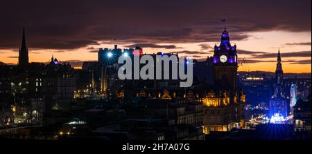 Edinburgh, Schottland, Großbritannien, 21st. November 2021. Castle of Light im Edinburgh Castle: Die Lichtshow von den Burgwällen kann über der Skyline der Hauptstadt mit einem farbenfrohen orangefarbenen Sonnenuntergangshimmel und den festlichen Lichtern des Weihnachtsmarktes auf der Princes Street gesehen werden Stockfoto