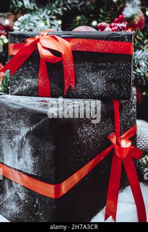 Schwarze Geschenkschachteln mit roten Schleifen, die mit Schnee bedeckt sind. Weihnachtliches festliches Konzept Stockfoto