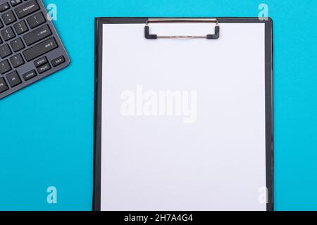 Schwarze Zwischenablage mit leerem weißen Blatt Papier auf blauem Tisch - Draufsicht, flach liegend Stockfoto