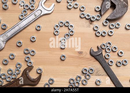 Fragezeichen aus Metallmuttern auf einem Holztisch, eine Vielzahl von Schraubenschlüsseln liegen in der Nähe. Problemlösungskonzept. Draufsicht. Stockfoto